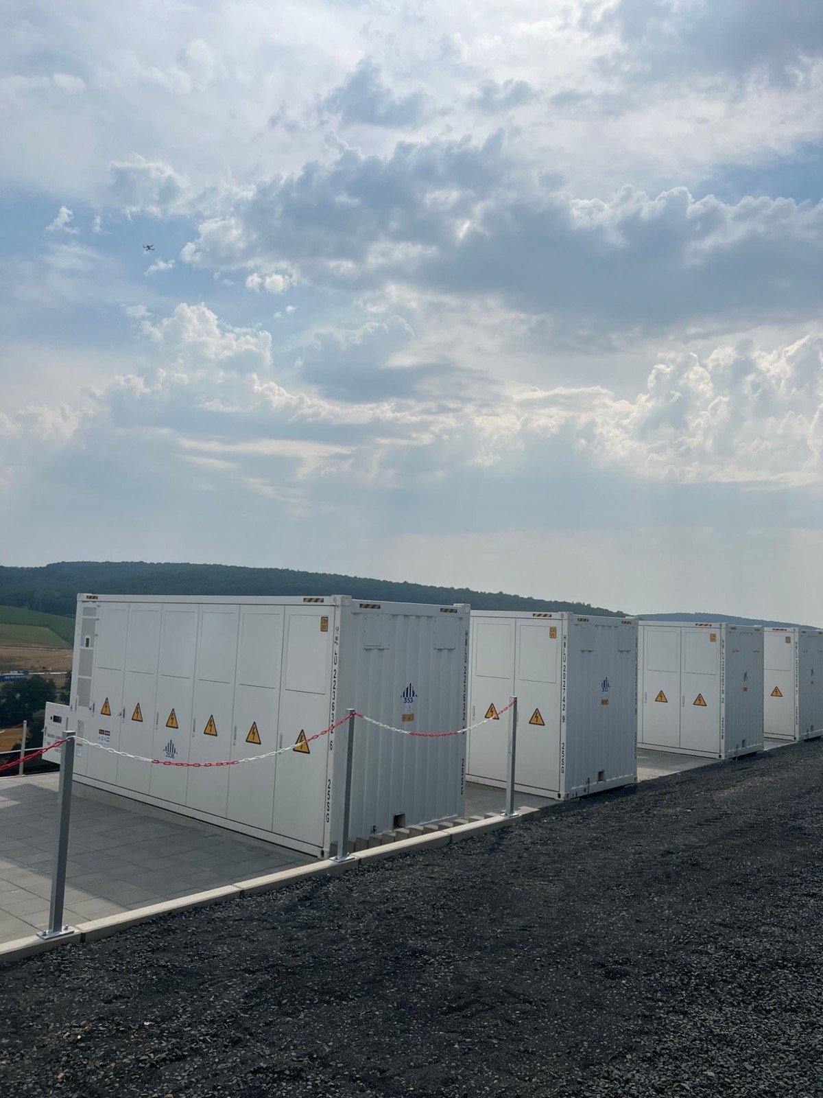 Reihe weißer Speichercontainer im Solarpark, darüber eine Drohne vor bewölktem Himmel
